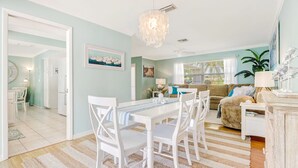 Un vaste espace de vie comprenant une table à manger, des chaises blanches, un canapé beige et un lustre.