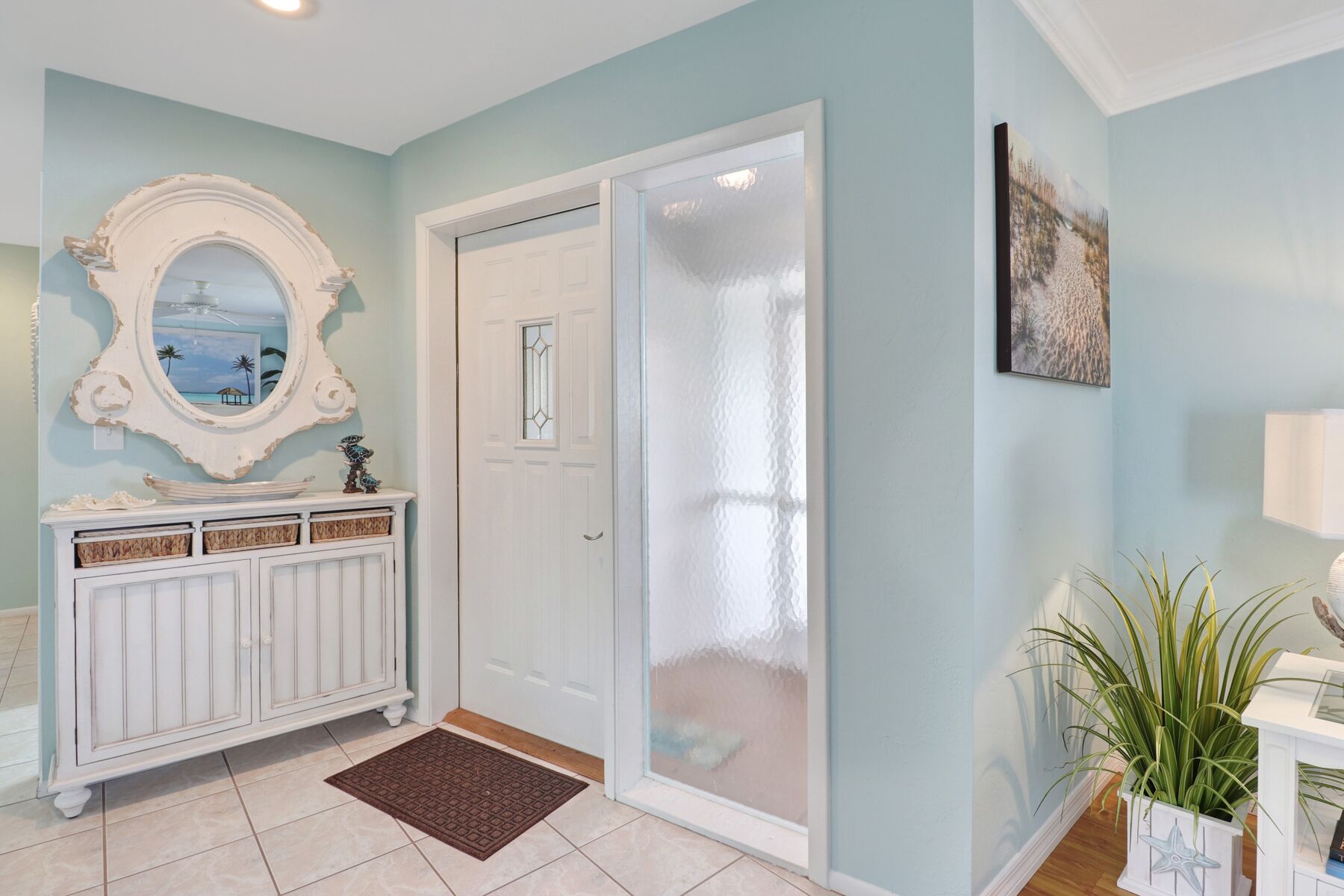 A room with a white door, a decorative mirror, a cabinet with baskets, a doormat, and a plant.
