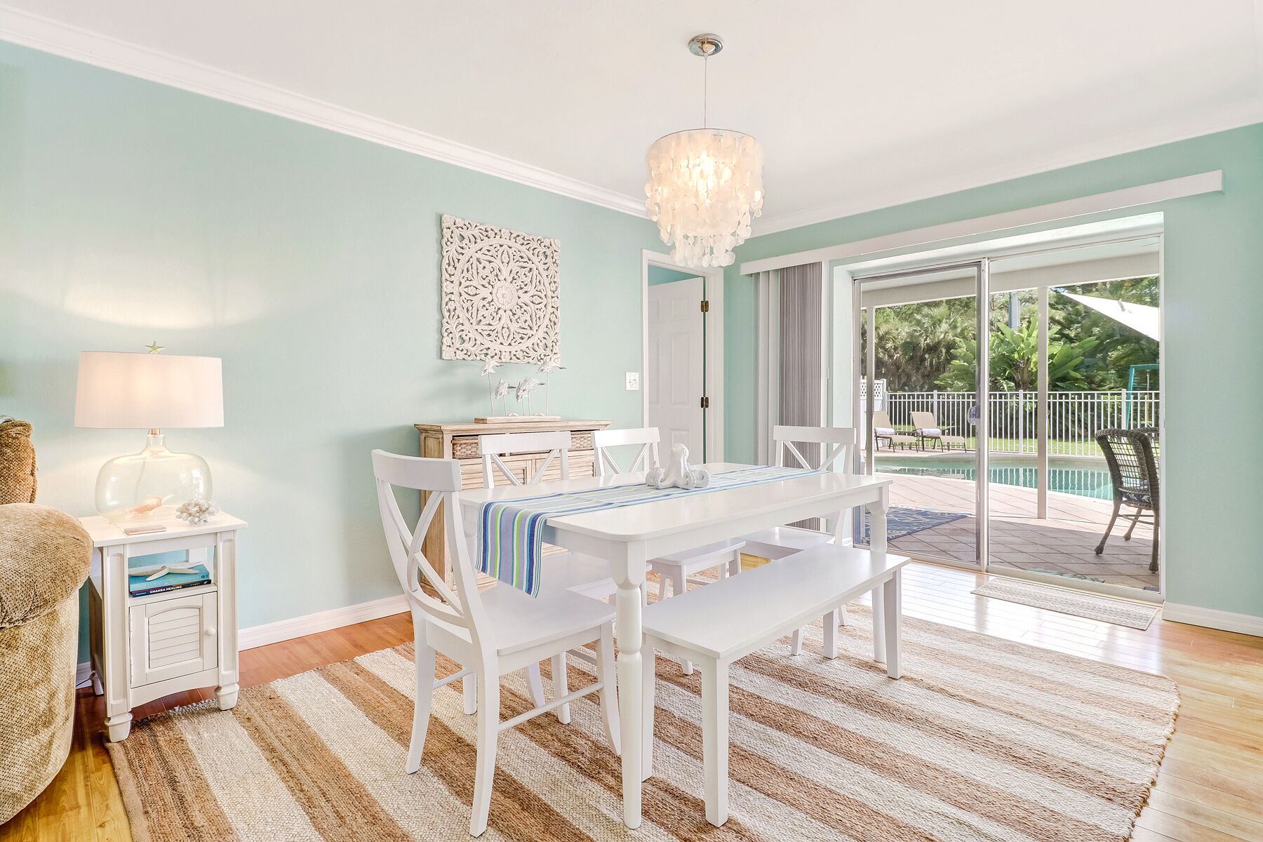 A dining area with a white table and chairs, a chandelier, and a view of a pool through glass doors.