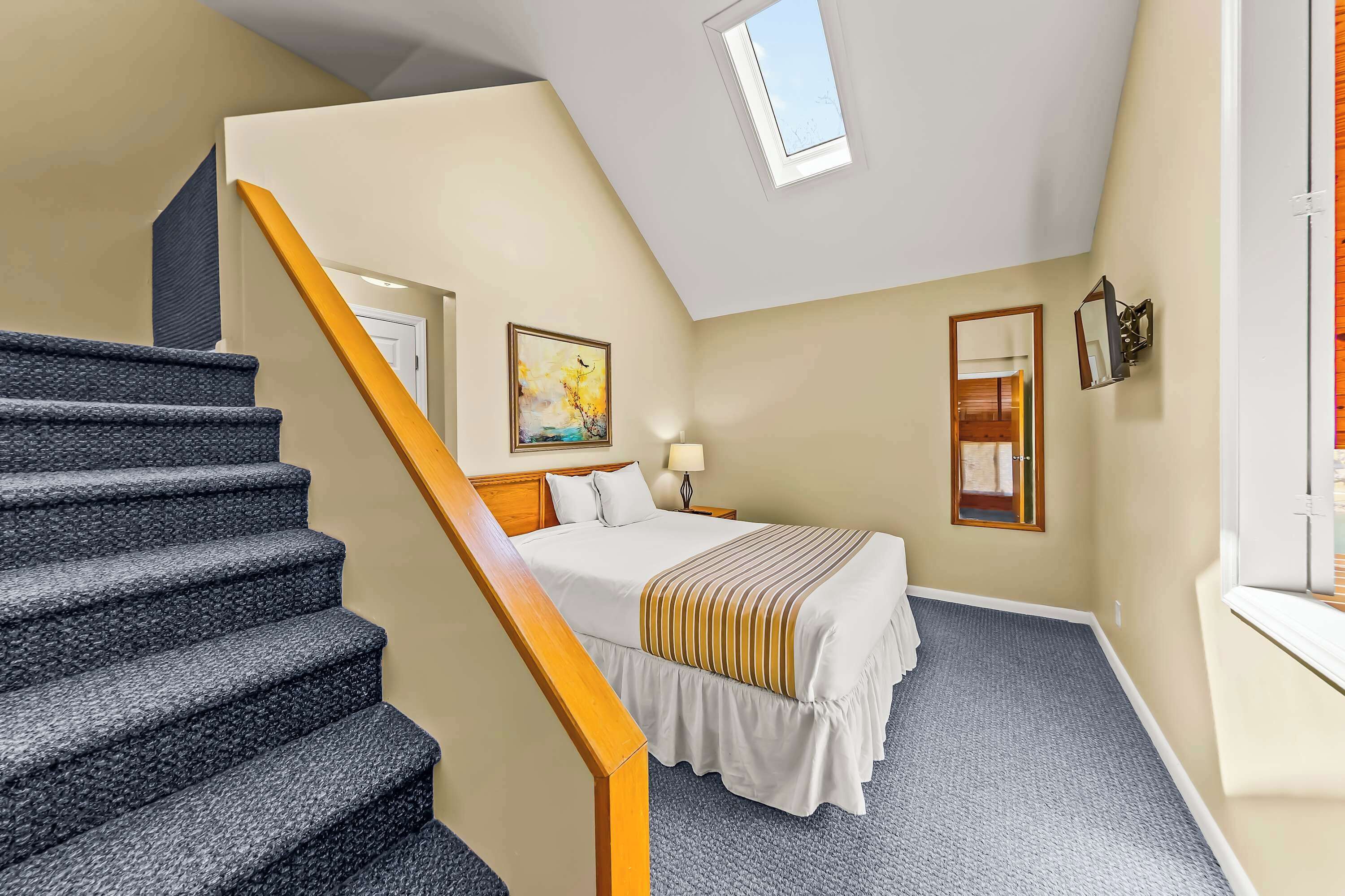 A bedroom with a bed, a nightstand, a lamp, a painting, a window, and a staircase.