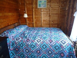 Ein Zimmer mit Holzboden, einem Bett, einer Hängelampe und einem gerahmten Bild an der Wand.