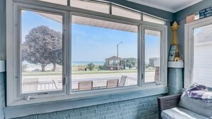 A room with a large window overlooking a beach, a wicker sofa, and a brick wall. - Enjoy Beachfront Living With family!  (Racine)