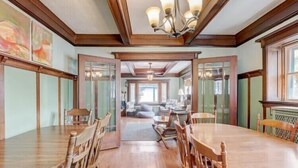 A spacious dining area with wooden tables and chairs, a chandelier, and a view into a living room with a sofa and coffee table. - Enjoy Beachfront Living With family!  (Racine)