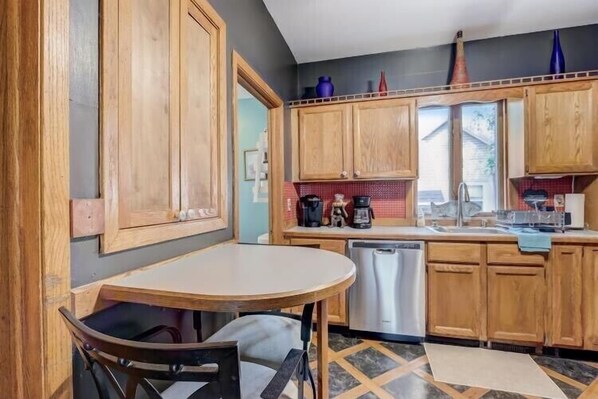 A compact kitchen with wooden cabinets, a dishwasher, and a small dining table.