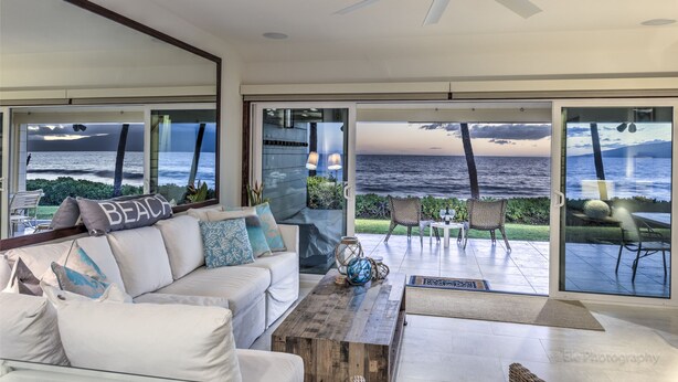 A modern living room with a large window overlooking the ocean, a ceiling fan, and a cozy seating area. - OCEANFRONT PUAMANA 136-1 - FUN IN THE SUN! (Lahaina)