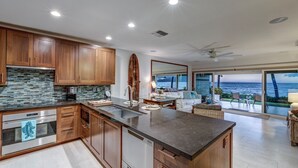 A modern kitchen with wooden cabinets, a stone backsplash, and a large island. - OCEANFRONT PUAMANA 136-1 - FUN IN THE SUN! (Lahaina)