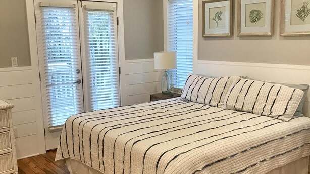 A bedroom with a large bed, wooden flooring, a ceiling fan, and framed botanical prints on the wall.