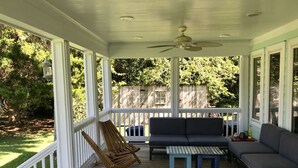 A covered porch with a ceiling fan, a sofa, a table, and two rocking chairs.