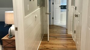 A hallway with white walls, wooden flooring, and a door leading to another room.