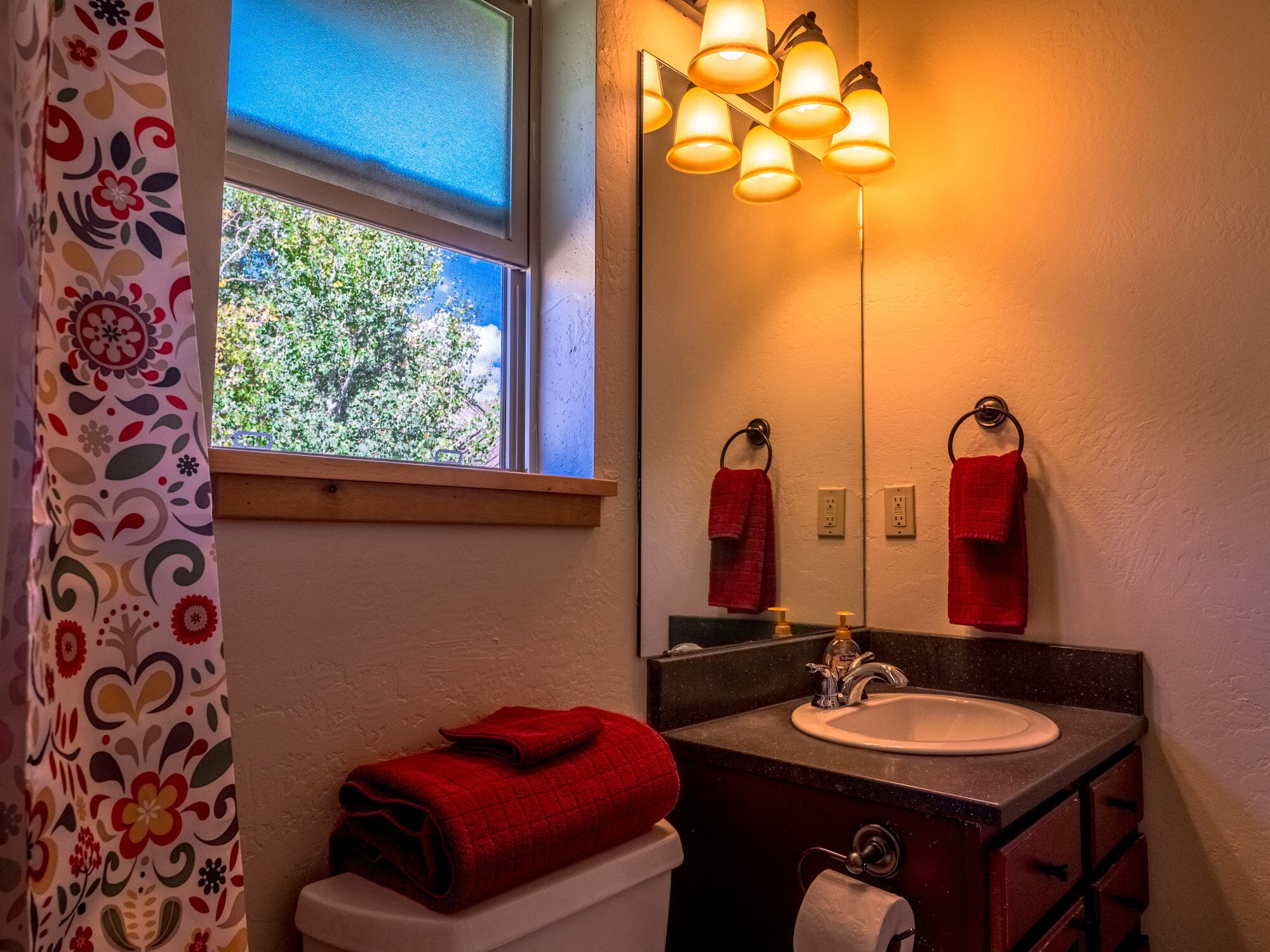A bathroom with a window, a sink, a toilet, and a mirror.