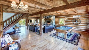 Interior espaiós d'una cabana de fusta amb una zona d'estar acollidora, taula de bitlles i una llar de pedra.