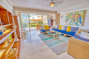 A spacious living room with a sofa set, a glass coffee table, and a view of the outdoor area through large sliding doors.