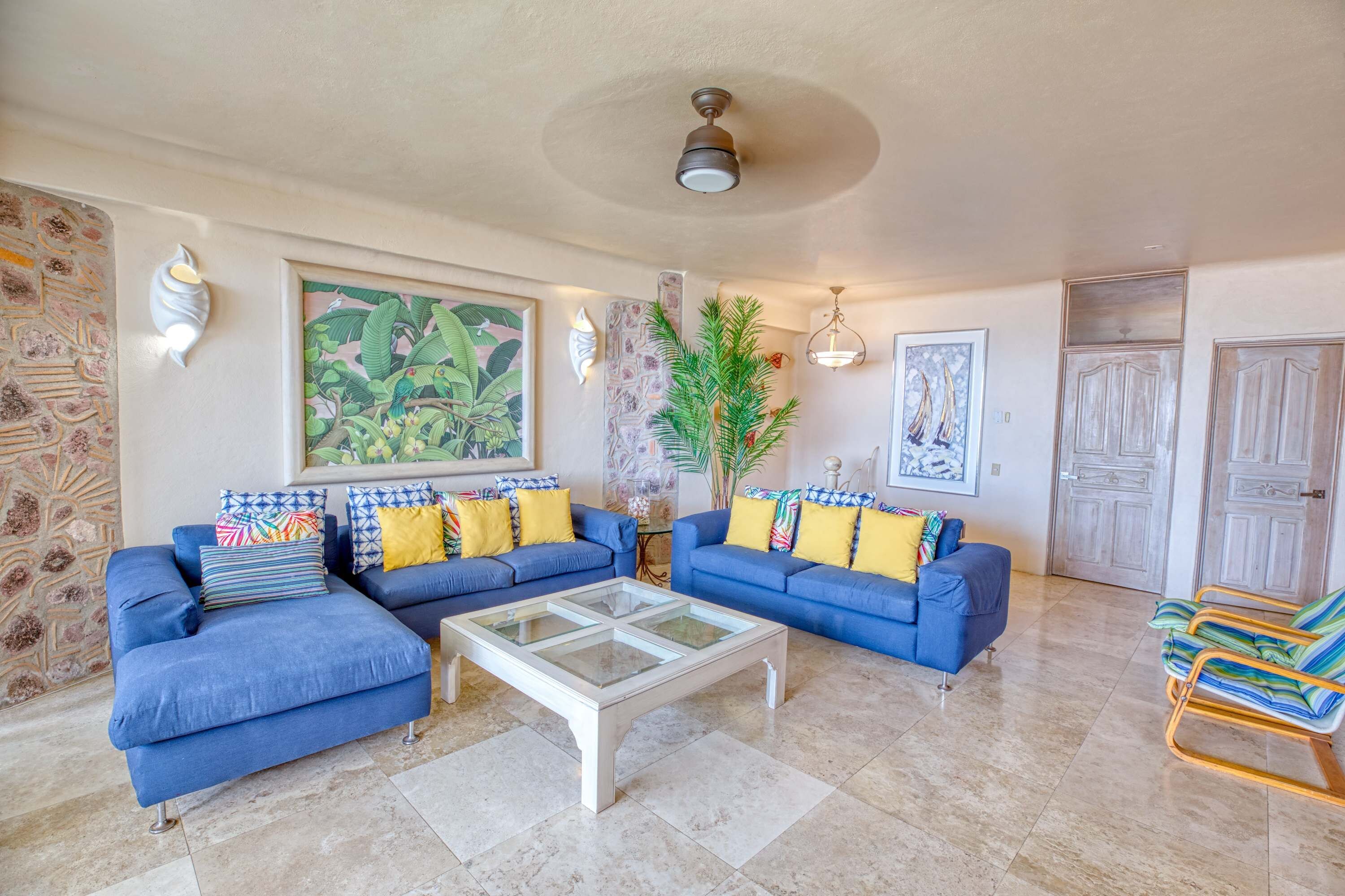 A living room with a sectional sofa, a glass coffee table, and a potted plant.