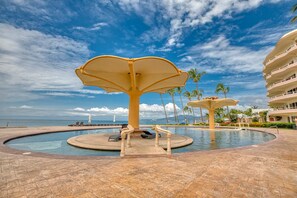 A pool area with a central fountain, palm trees, and a view of the ocean.