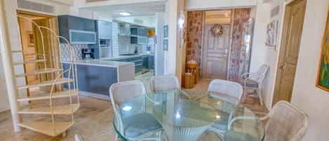 A modern kitchen with white cabinetry, a central island, and a dining area with a glass table and wicker chairs.