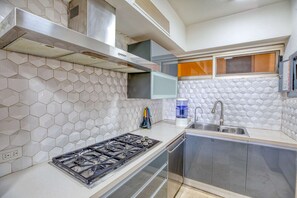 A modern kitchen with a gas stove, stainless steel cabinets, a sink, and a hexagonal tile backsplash. - Beachfront 3-bedroom condo with pool (Nuevo Vallarta)