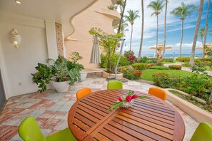 A round wooden table with chairs, surrounded by potted plants and a view of the ocean.