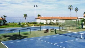 An outdoor tennis court with multiple courts, surrounded by palm trees and a building with a red roof. - DELUXE VILLA FOR 6 GUESTS-2 BEDROOM,1BATH (Rosarito)