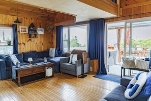 A cozy living room with wooden walls, a sofa set, a coffee table, and a view of the outdoors. - Ocean View • Hot Tub • Pet-Friendly Coastal Retreat (Parrsboro)