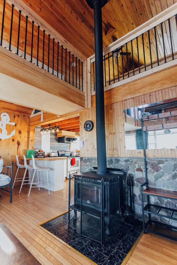 A wooden interior with a stone fireplace, a kitchen area, and a seating area with chairs.