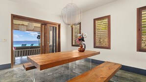 Ein Essbereich mit einem Holztisch, transparenten Glasbeinen und Meerblick durch eine Tür.