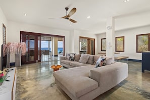 A spacious living area with a large sectional sofa, a ceiling fan, and a view of the ocean through large windows.