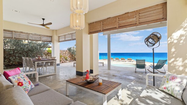 Ein großzügiger Wohnbereich mit einem Holztisch, einer Couch und Blick auf den Strand.