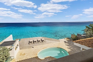 A pool area with a view of the sea, lounge chairs, and a wooden deck.