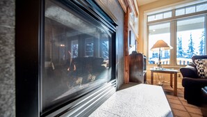 A cozy room with a fireplace, a window with a view of trees, and a lamp on a side table.