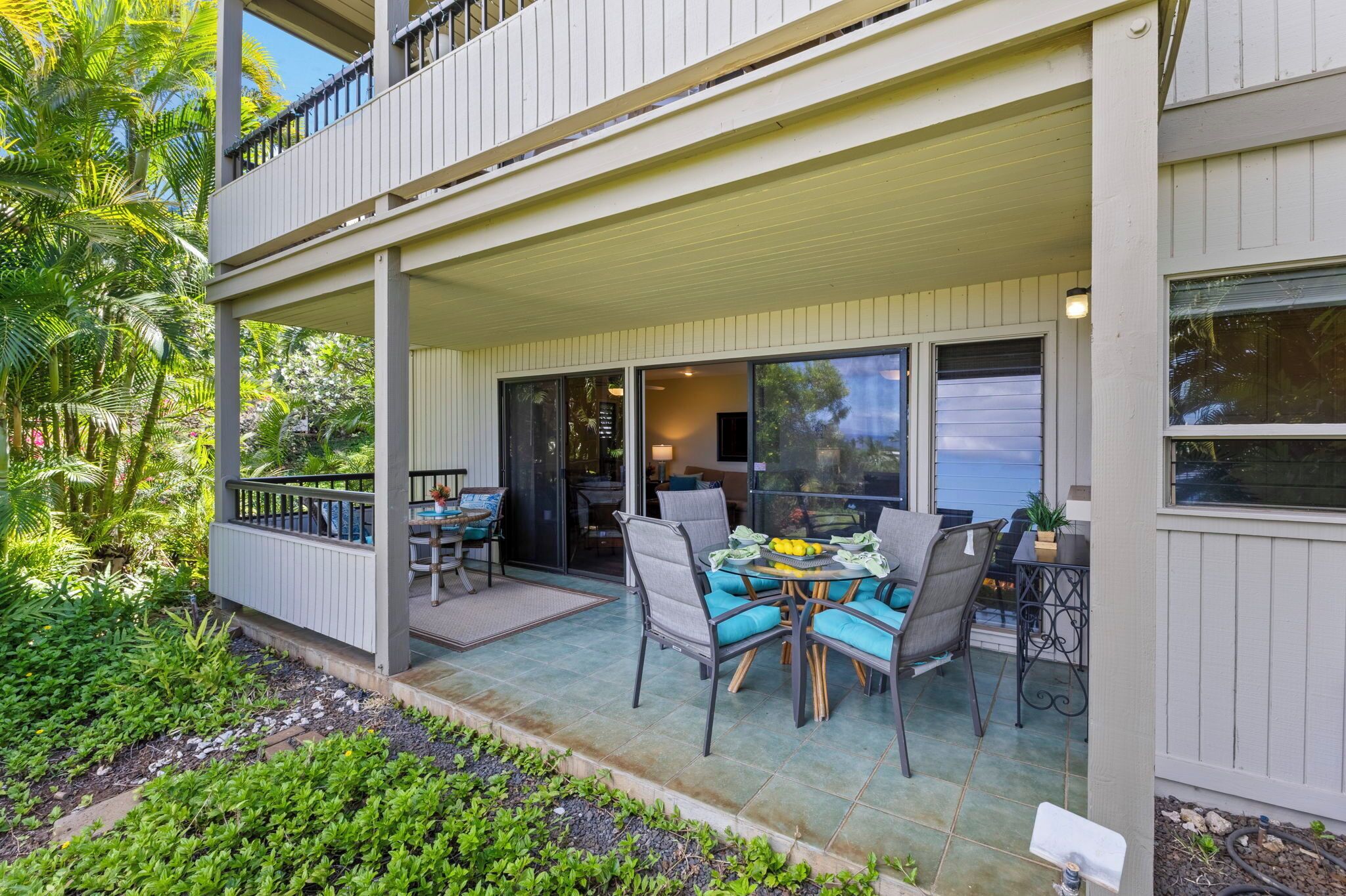 A covered outdoor patio with a dining table and chairs, surrounded by lush greenery.