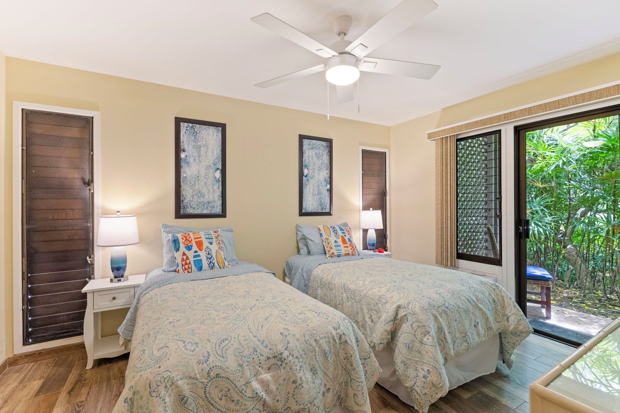 A bedroom with two beds, a ceiling fan, and a sliding glass door to a garden.