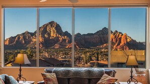 A living room with a large window offering a view of a mountain range. - Spectacular Red Rock Views from Gorgeous Pueblo-style Sedona Home with hot tub! (Sedona)