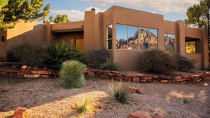 A modern house with a desert landscape view, featuring a stone wall and native plants. - Spectacular Red Rock Views from Gorgeous Pueblo-style Sedona Home with hot tub! (Sedona)