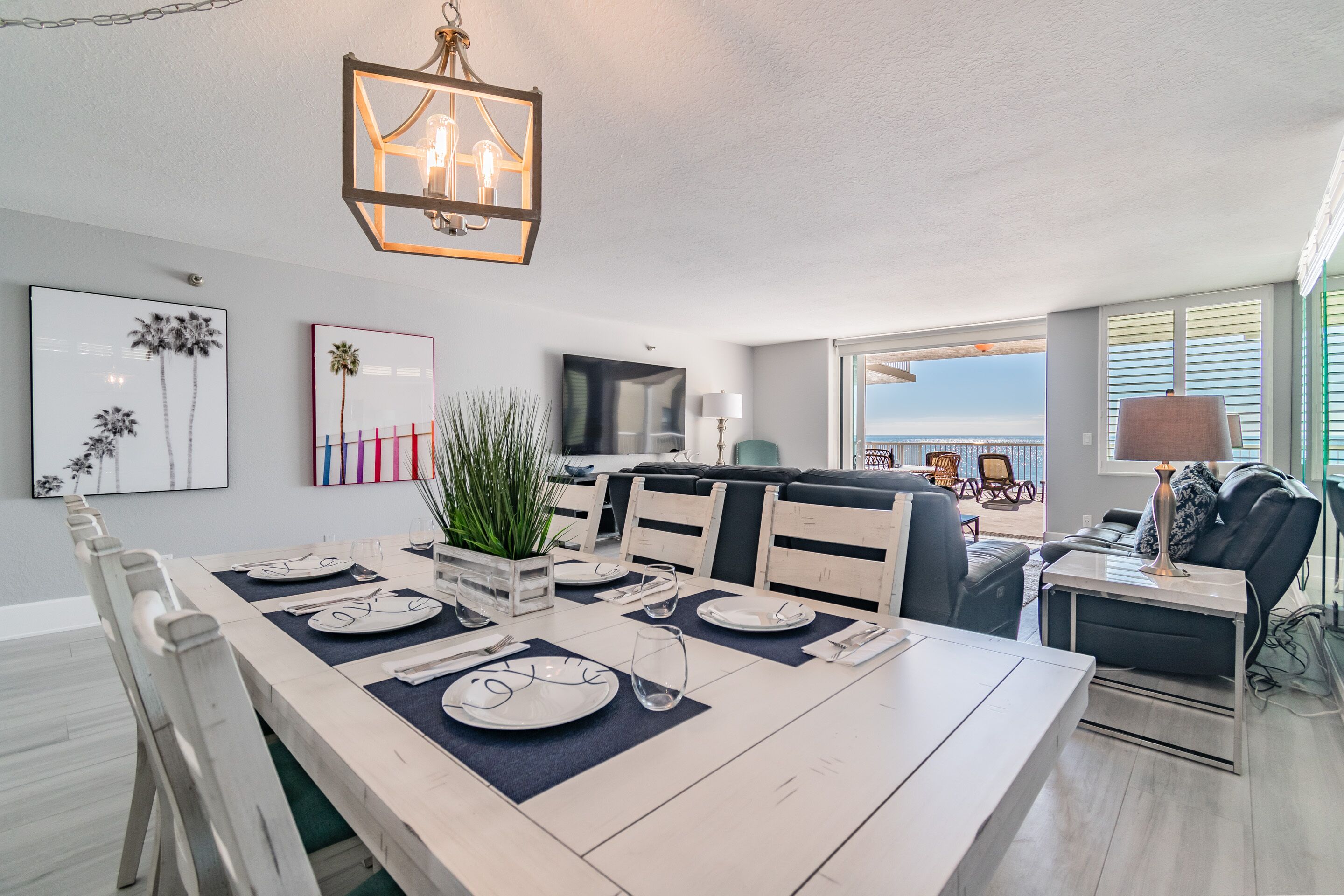 A dining area with a long table set for four, a television in the background, and a view of the outdoors.