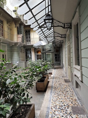 A covered corridor with tiled flooring, potted plants, and a glass ceiling.