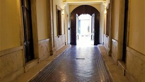 Käytävän lattia on laatoitettu, siinä on kaarevat oviaukot ja seinään kiinnitetyt valaisimet.