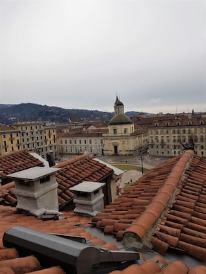 A cityscape with terracotta-tiled rooftops, a prominent church with a green dome, and surrounding buildings.