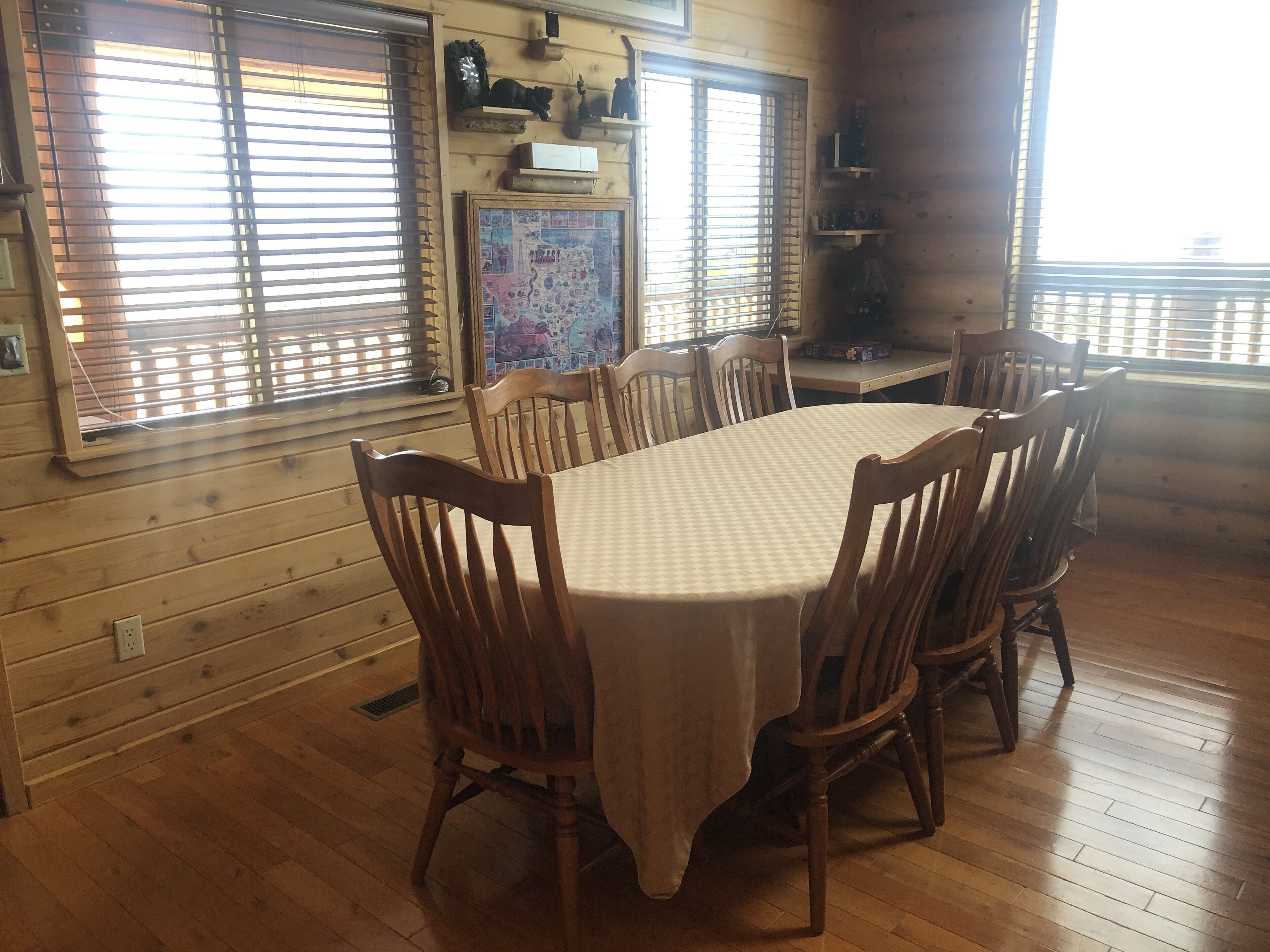 A dining area with a wooden table and chairs, a window with blinds, and a wall-mounted shelf with various items.