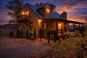 Una casa in legno a due piani con un balcone, un portico coperto e montagne sullo sfondo.