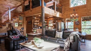 Eine geräumige Holzhütte mit Schlafzimmer im oberen Bereich, einem Essbereich und einem gemütlichen Wohnzimmer, möbliert mit Ledersofas und einem Couchtisch.