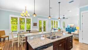 Una cocina amplia con encimeras de granito, lavavajillas y una isla grande. Hay varias ventanas que proporcionan luz natural y vistas al exterior.