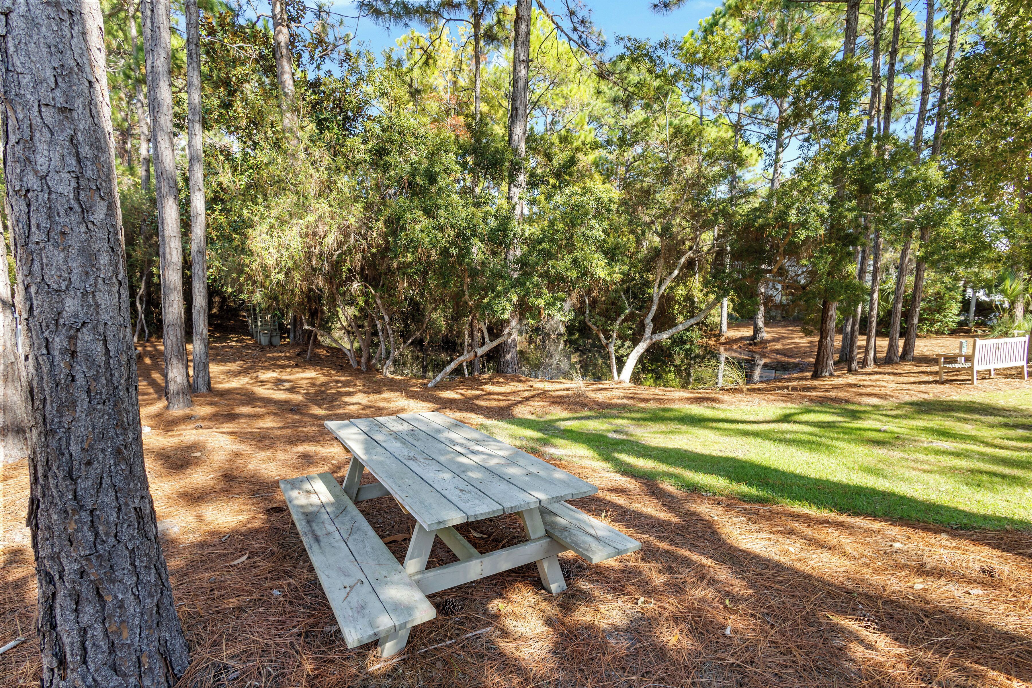 Une table de pique-nique située dans un espace boisé, avec des arbres et de l’herbe.