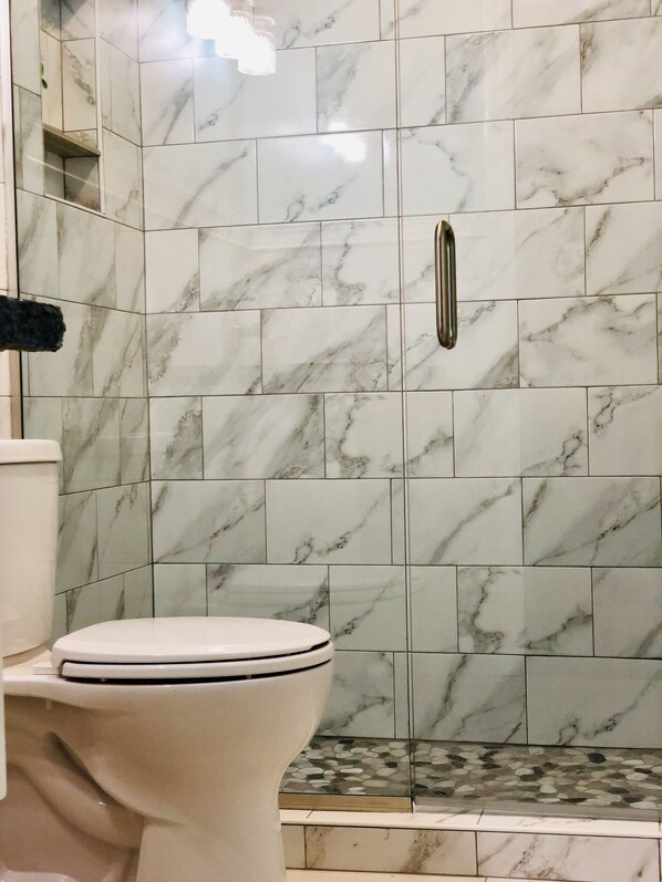 A bathroom with a toilet, a shower area with marble tiles, and a handrail.
