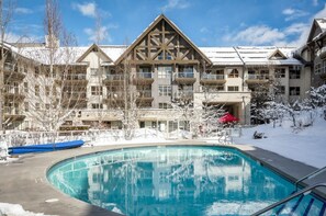 A hotel with a pool, snow-covered surroundings, and a large building with multiple balconies. - True Ski in/Ski Out Location- Renovated with Terrific Mountain Views (Whistler)