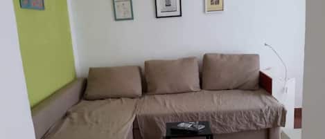 A living room with a sofa and a small table, a green wall, and three framed pictures on the wall.