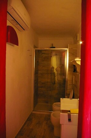 Ein kleines Badezimmer mit Duschkabine aus Glas, Toilette und weißem Waschbecken mit Spiegel.