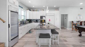 Een moderne keuken met witte kasten, een marmeren eiland en een pooltafel.
