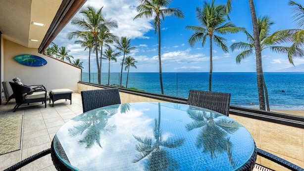 A glass-top table with wicker chairs, a sofa, and a view of the ocean with palm trees. - Beachfront Condo E 303/ Incredible views/ Pickleball/Great Snorkeling (Kihei)