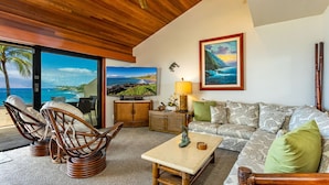 A room with a wooden ceiling, a sofa, a coffee table, wicker chairs, a TV, and a view of the ocean. - Beachfront Condo E 303/ Incredible views/ Pickleball/Great Snorkeling (Kihei)
