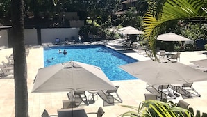 A swimming pool with lounge chairs and umbrellas, surrounded by palm trees and a tiled patio area. - Beachfront Condo E 303/ Incredible views/ Pickleball/Great Snorkeling (Kihei)